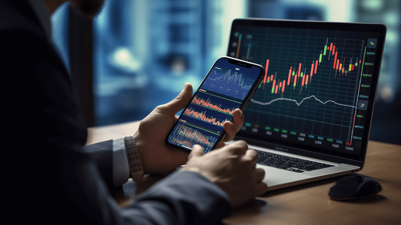 uomo con pc e telefono che controlla grafici